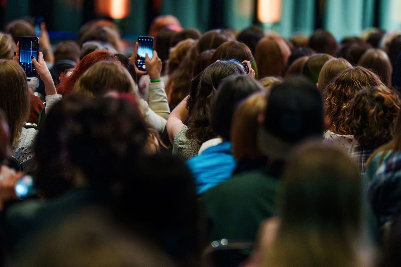 Large audience of people holding smartphones, recording and photographing an event or presentation.