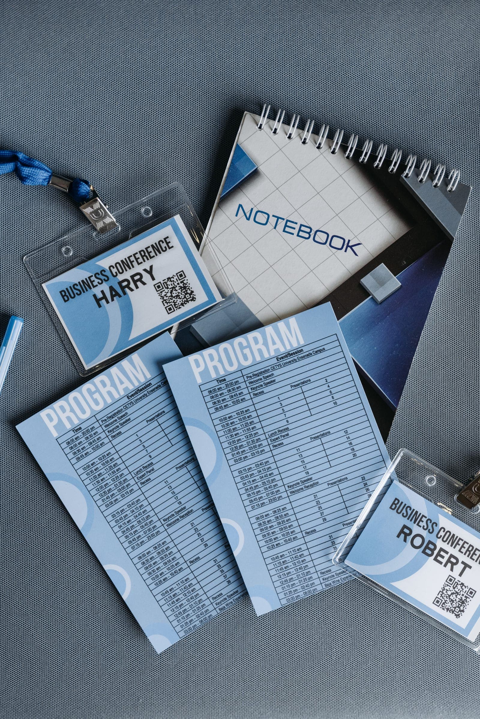 Overhead view of organized conference materials including badges with lanyards, program schedules, and spiral notebooks on gray table.
