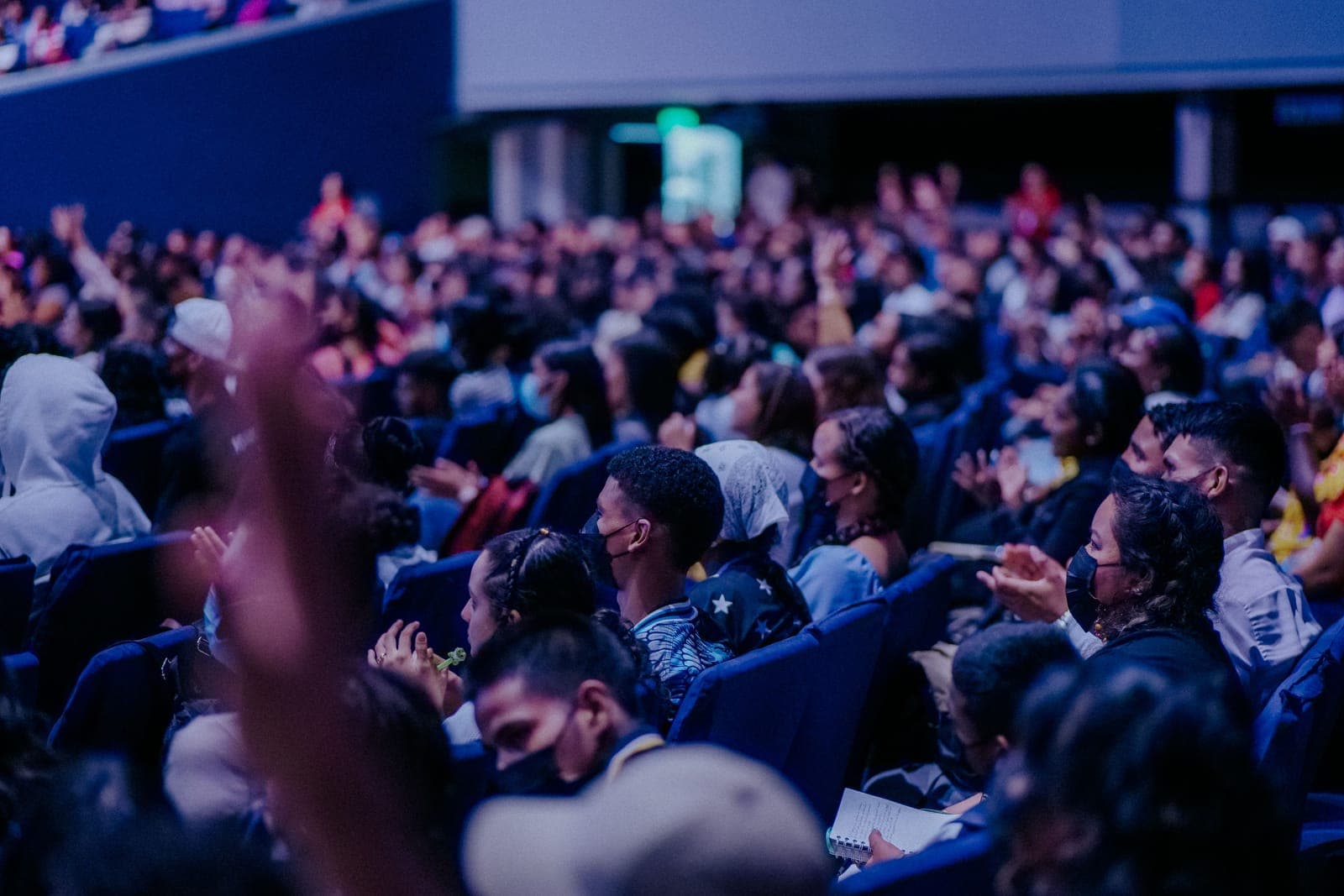 Wide view of a large conference audience seated in an auditorium facing a stage with professional lighting.