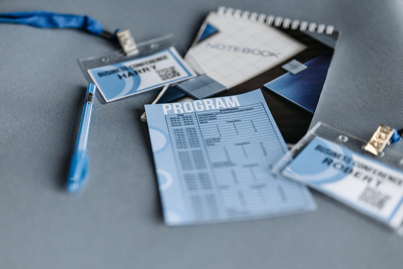 Flat lay of a blue conference badge with lanyard, program documents, and notepads scattered on gray surface.