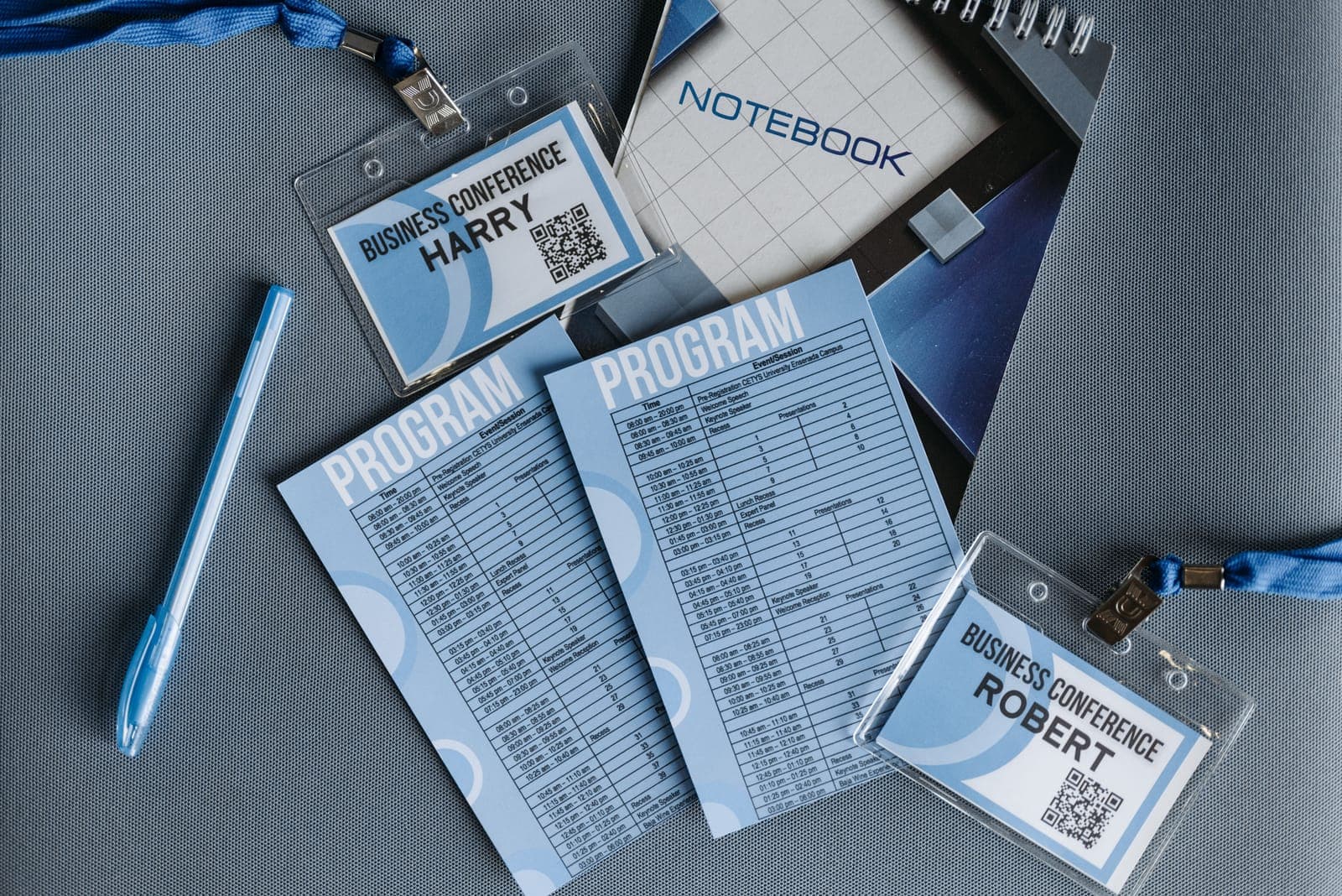 Flat lay arrangement of conference materials including badges, lanyards, program handouts, and notebooks with blue accent color.