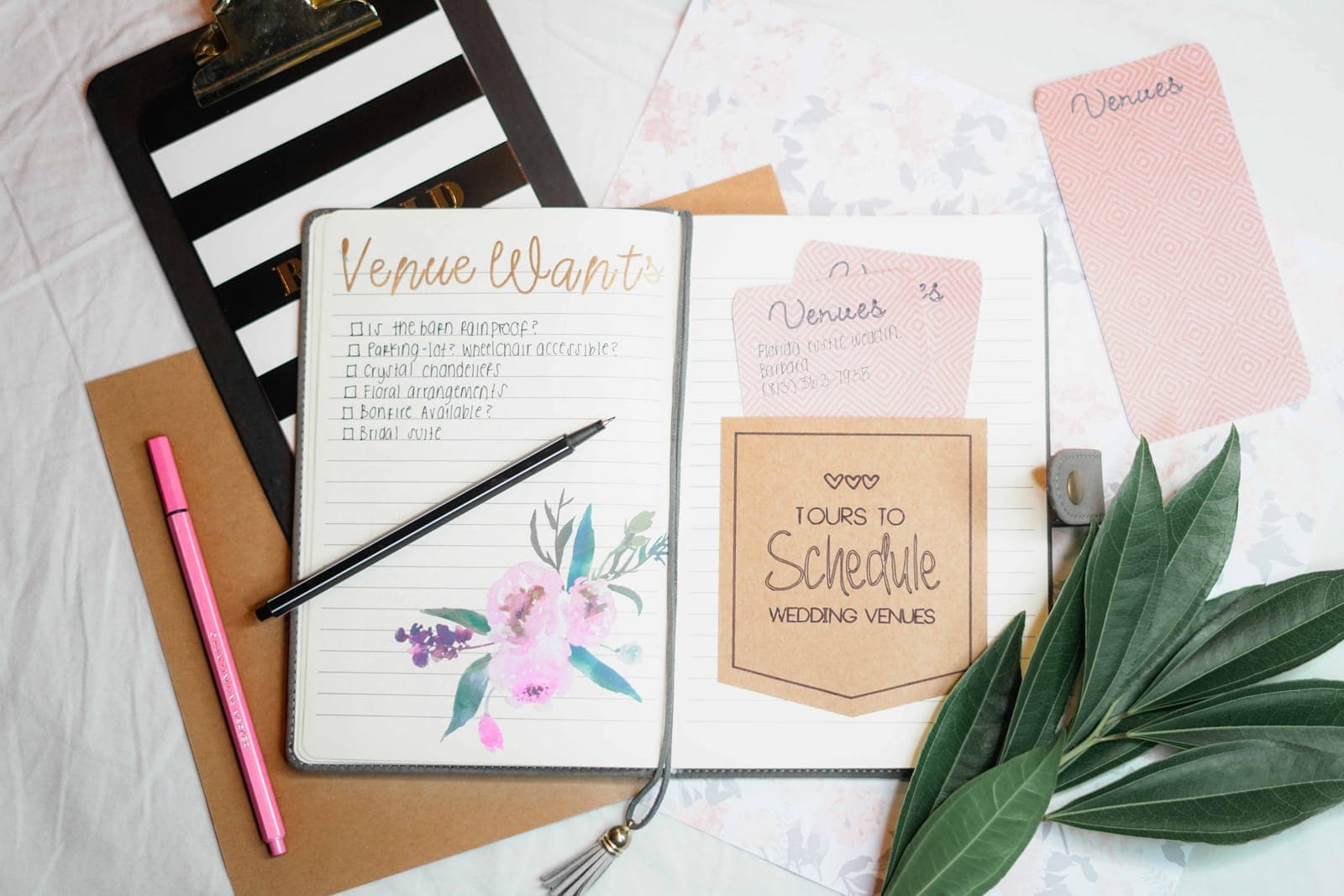 Flat lay of event planning documents including venue checklists, schedule planning cards, and decorative elements on a white surface.