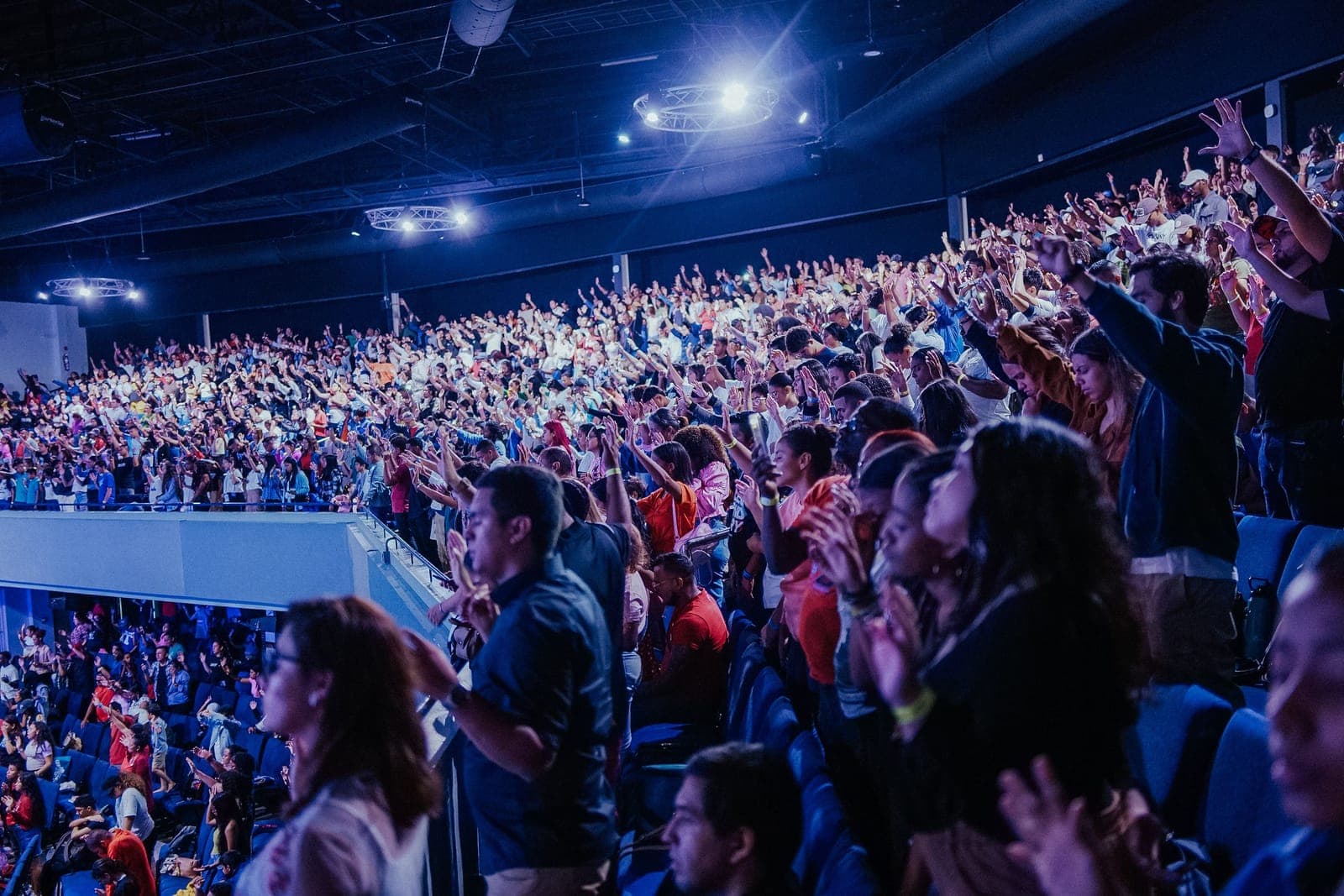 Massive crowd in a large venue with professional stage lighting and thousands of attendees.