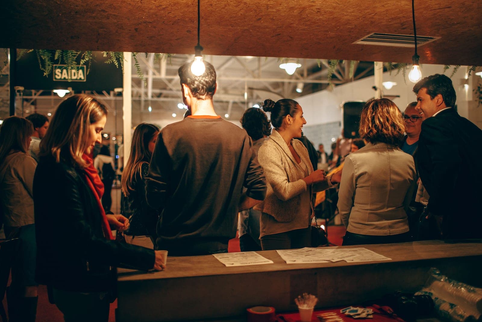 Attendees standing and talking around a counter at an informal networking event, with printed handouts on the surface.