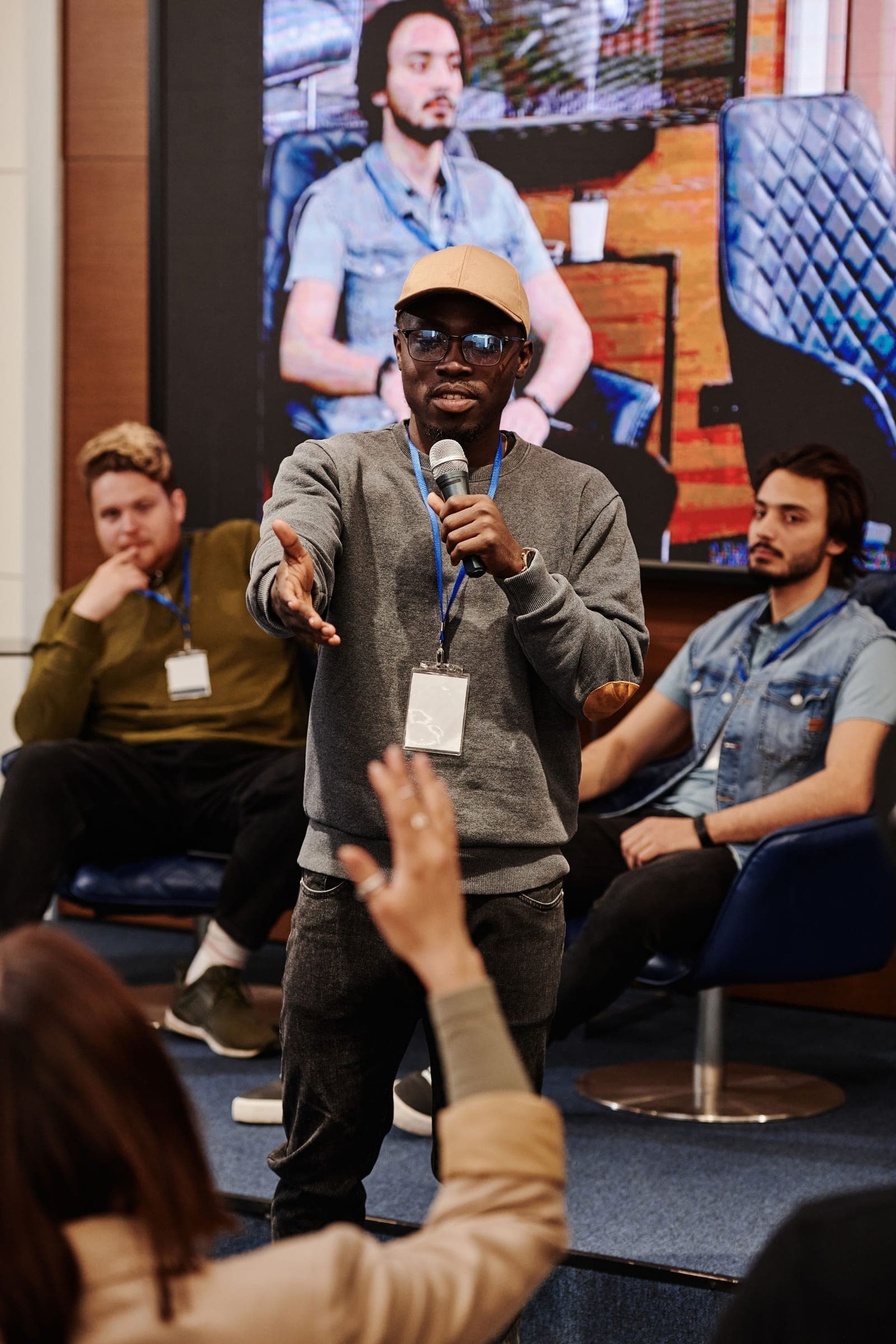 Man wearing sunglasses speaks into a microphone at a panel discussion with attendees seated around him.