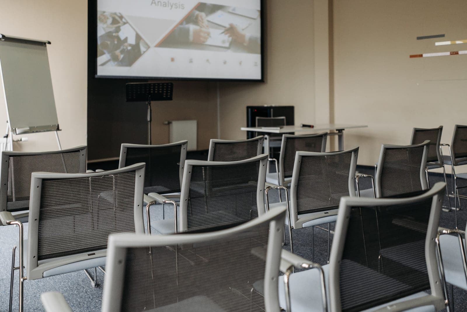 Empty conference room with rows of black mesh chairs facing a projection screen displaying a business analysis presentation.